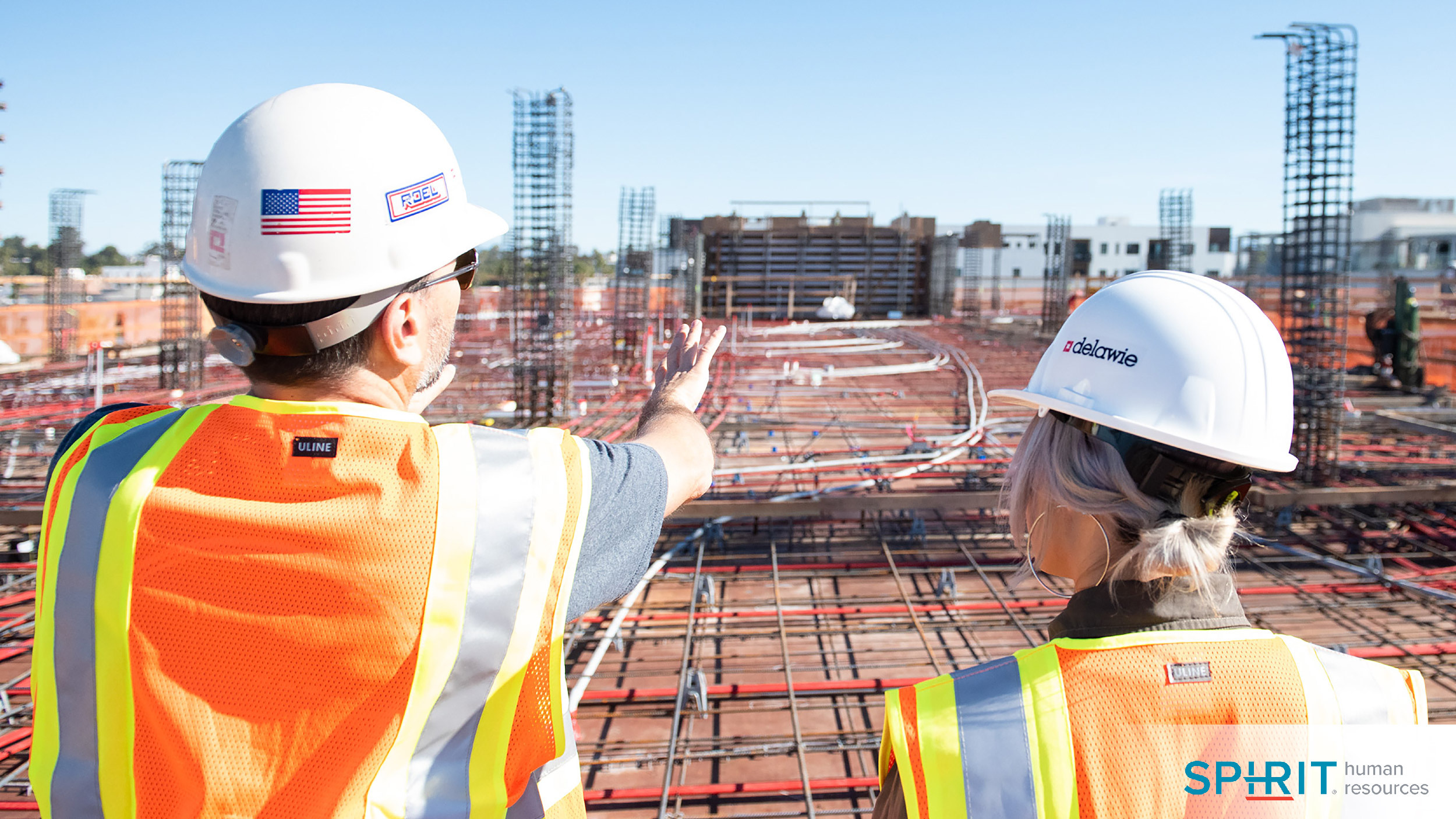 two workers in safety vests and helmets looking over a job site